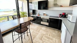 A modern kitchen with a view of the sea, a dining area with a table and chairs, and a large window. - Luxury T3 standing 2 - Vue mer exceptionnelle 180° (Larmor-Plage)