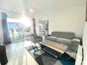 A modern living room with a grey sofa, a wooden coffee table, and a glass dining table with chairs.