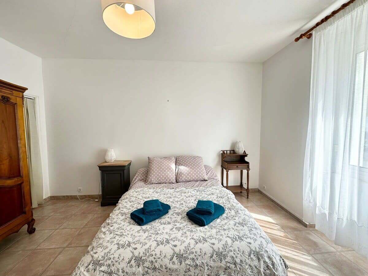 A bedroom with a bed, two bedside tables, a wooden wardrobe, and a window with curtains.