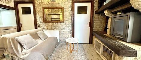 Una habitación acogedora con pared de piedra, un sofá, una mesita redonda, un televisor y una chimenea.