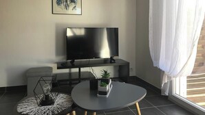 Una sala de estar moderna con un televisor de pantalla plana, una mesa de centro redonda y una mesita auxiliar con adornos.