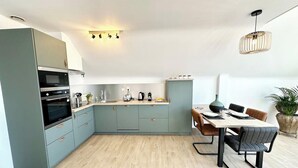 Une cuisine moderne avec des meubles gris, un plan de travail en bois et un coin repas comprenant une table et des chaises.