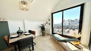 Un espace repas moderne avec une table dressée pour deux personnes, un banc et une grande fenêtre donnant sur la ville.