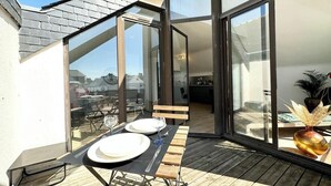 Un coin repas avec une table dressée pour deux personnes, de grandes fenêtres et une vue sur la ville.