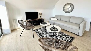 Un salon moderne comprenant un canapé, deux fauteuils, une table basse et un téléviseur.