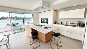 A modern kitchen with a large island, white cabinetry, and a view of the sea.