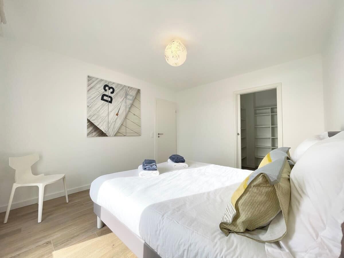 A bedroom with a bed, a chair, a wardrobe, and a wall-mounted artwork.