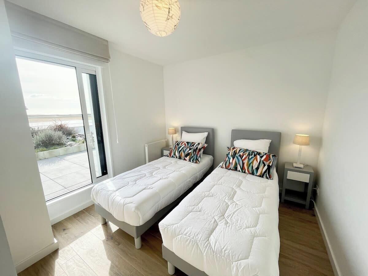 Ein Schlafzimmer mit zwei Betten, einem großen Fenster und einem Balkon.
