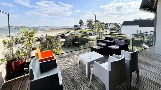 Un balcon avec des sièges pour l’extérieur, une vue sur la plage et des plantes en pot.