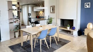 Une cuisine moderne avec des meubles blancs, un four encastré et un coin repas comprenant une table en bois et des chaises bleues.