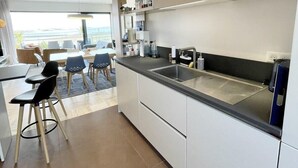 Une cuisine moderne dotée d’un grand îlot central, d’appareils électroménagers intégrés et offrant une vue sur l’extérieur.