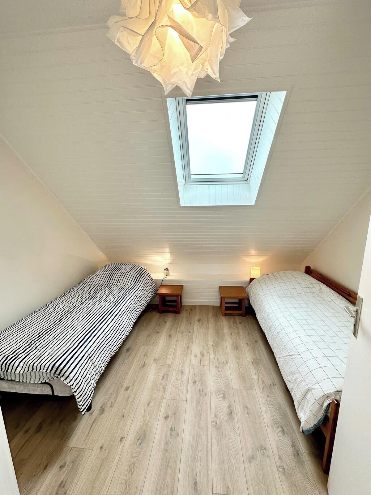 A small, well-lit room with two single beds, a skylight, and a wooden floor.