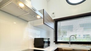 Una cocina moderna con microondas incorporado, extractor de acero inoxidable y ventana con persianas.