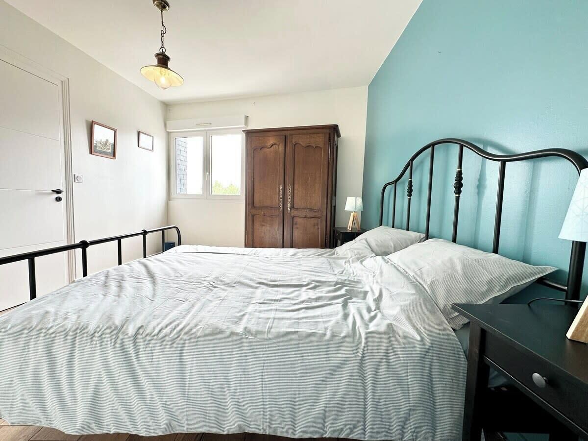 A bedroom with a bed, a nightstand, a wardrobe, and a window.