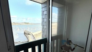 Une pièce dotée d’une grande fenêtre donnant sur une plage, d’un plancher en bois et d’une porte menant à un balcon.