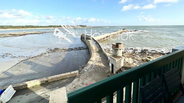 Une vue sur la côte, avec une jetée en pierre menant à une plage rocheuse, un ciel dégagé et une mer calme.