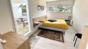 A modern bedroom with a bed, a small desk, a chair, and a view of the outdoors. - Charmant T2 Top Cosy Face à la rade (Larmor-Plage)