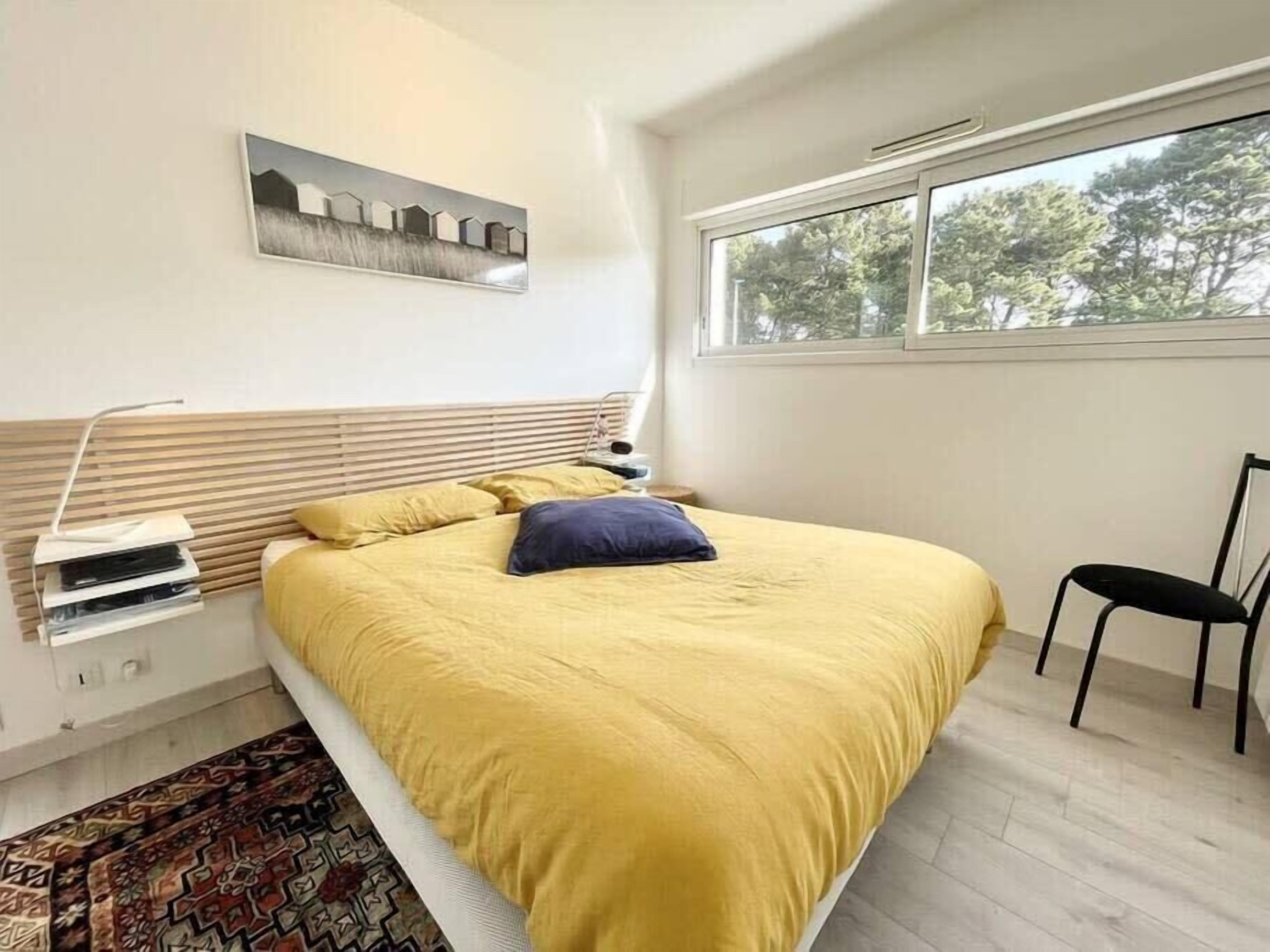 A bedroom with a bed, a window, a chair, and a painting on the wall.