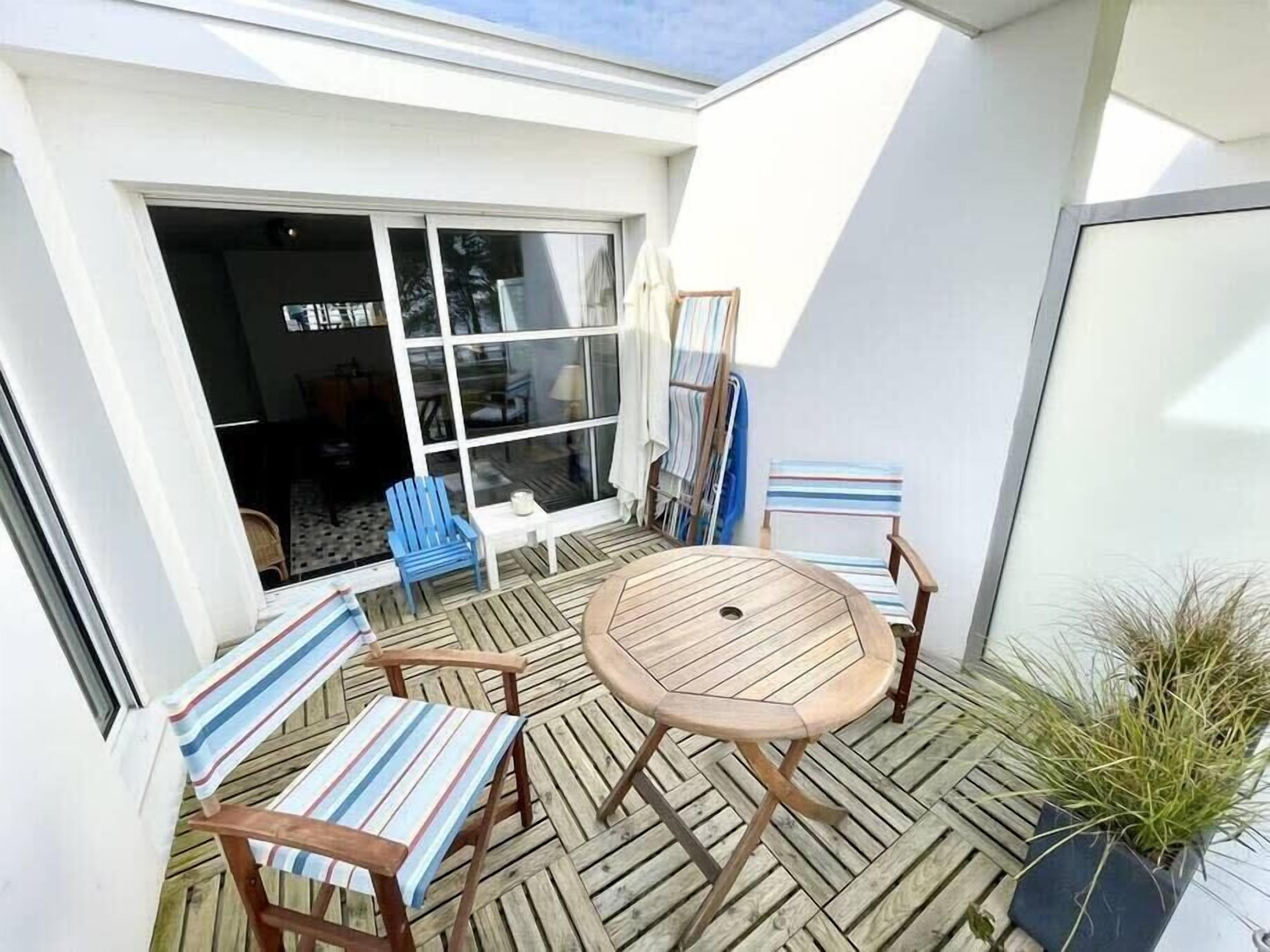 Un patio con una mesa de madera y sillas a rayas, un ventanal grande y una planta en maceta.