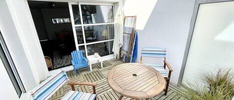Un patio con una mesa de madera y sillas a rayas, un ventanal grande y una planta en maceta.
