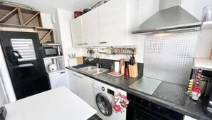 A compact kitchen with a washing machine, microwave, and a stainless steel range hood. - Charmant T2 Top Cosy Face à la rade (Larmor-Plage)