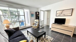 A modern living room with a sofa, coffee table, and a TV on a wooden cabinet. - Charmant T2 Top Cosy Face à la rade (Larmor-Plage)