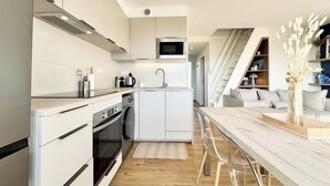 Una cucina moderna con mobili bianchi, un forno a microonde, un lavello e un tavolo da pranzo in legno con sgabelli da bar.