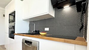A modern kitchen with white cabinetry, a black backsplash, and a wooden countertop.