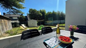 An outdoor patio with a table set for two, featuring a bottle of wine, glasses, and a bowl of cherry tomatoes.