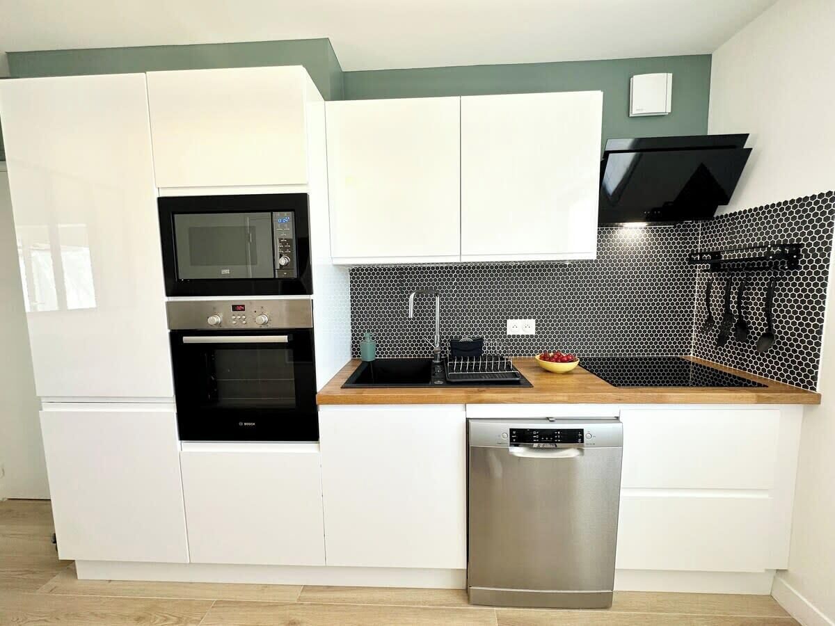A modern kitchen with white cabinets, a black microwave, a stainless steel dishwasher, and a honeycomb-patterned backsplash.
