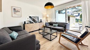 A modern living room with a sofa, a coffee table, and a chair. There is a TV on a stand and a window with curtains.