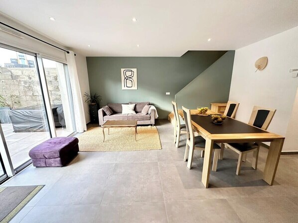 Una sala moderna con un sofá, una mesa de comedor y sillas. Hay un ventanal y una puerta que da al exterior.