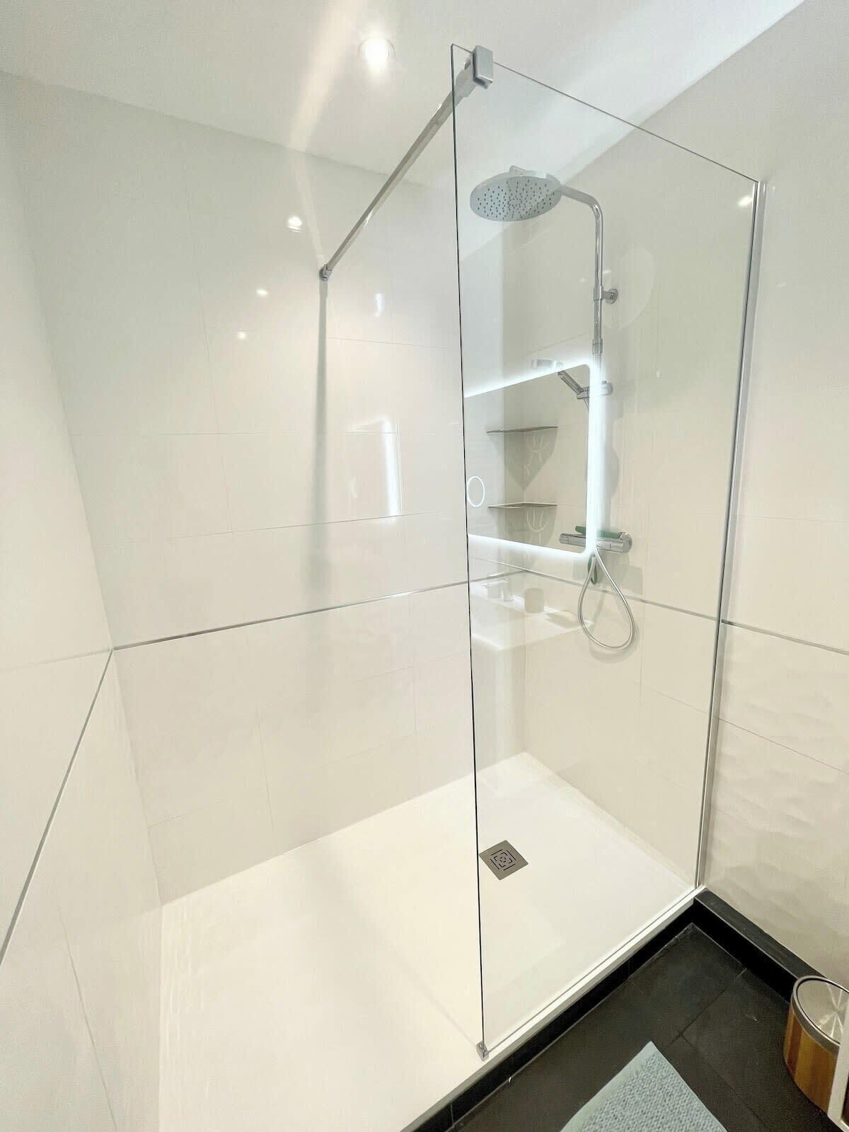 Een moderne badkamer met een douche met glazen wand, witte tegels en een zwarte vloer.
