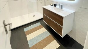 Ein modernes Badezimmer mit Duschkabine aus Glas, einem Waschtisch mit Spiegel und einem Streifen Teppichboden.