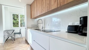 Eine moderne Küche mit weißen Schränken, einer Holz Arbeitsplatte, einer schwarzen Kaffeemaschine und einem Fenster mit Grünpflanzen draußen.