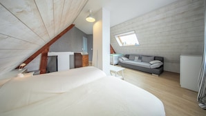 A bedroom with a large bed, a small table, a sofa, a desk, and a window.