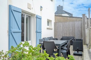 Une terrasse avec une table et des chaises, une clôture en bois et un bâtiment aux volets bleus.