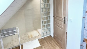A small, sloped ceiling room with a wooden door, a white radiator, and a glass partition.