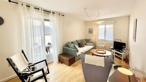 A living room with a sofa, a chair, a small table, a TV, and a window with curtains.