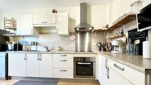 A modern kitchen with white cabinets, a stainless steel range hood, and a built-in oven.
