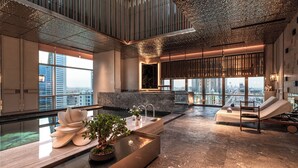 Un espace piscine intérieur moderne, doté d’une grande baie vitrée, d’un coin salon et d’un fauteuil de massage.