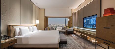 A hotel room with a large bed, a desk with a computer, a TV, and a view of the city.