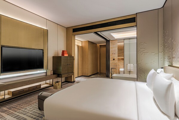Una habitación de hotel moderna con una cama grande, un televisor de pantalla plana, un armario de madera y un baño con espejo y toallero.