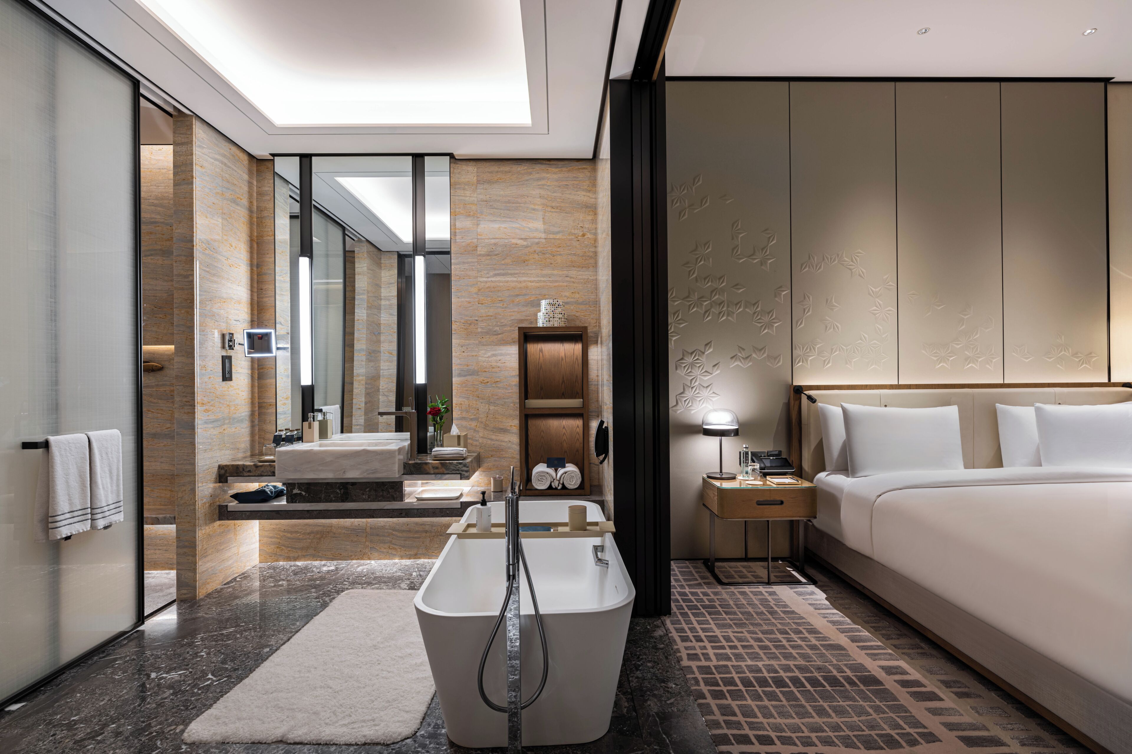 A modern hotel room with a large bed, a separate bathroom with a bathtub, a vanity with a mirror, and a walk-in closet.