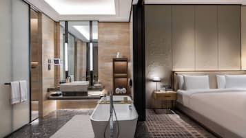 A modern hotel room with a large bed, a separate bathroom with a bathtub, a vanity with a mirror, and a walk-in closet.