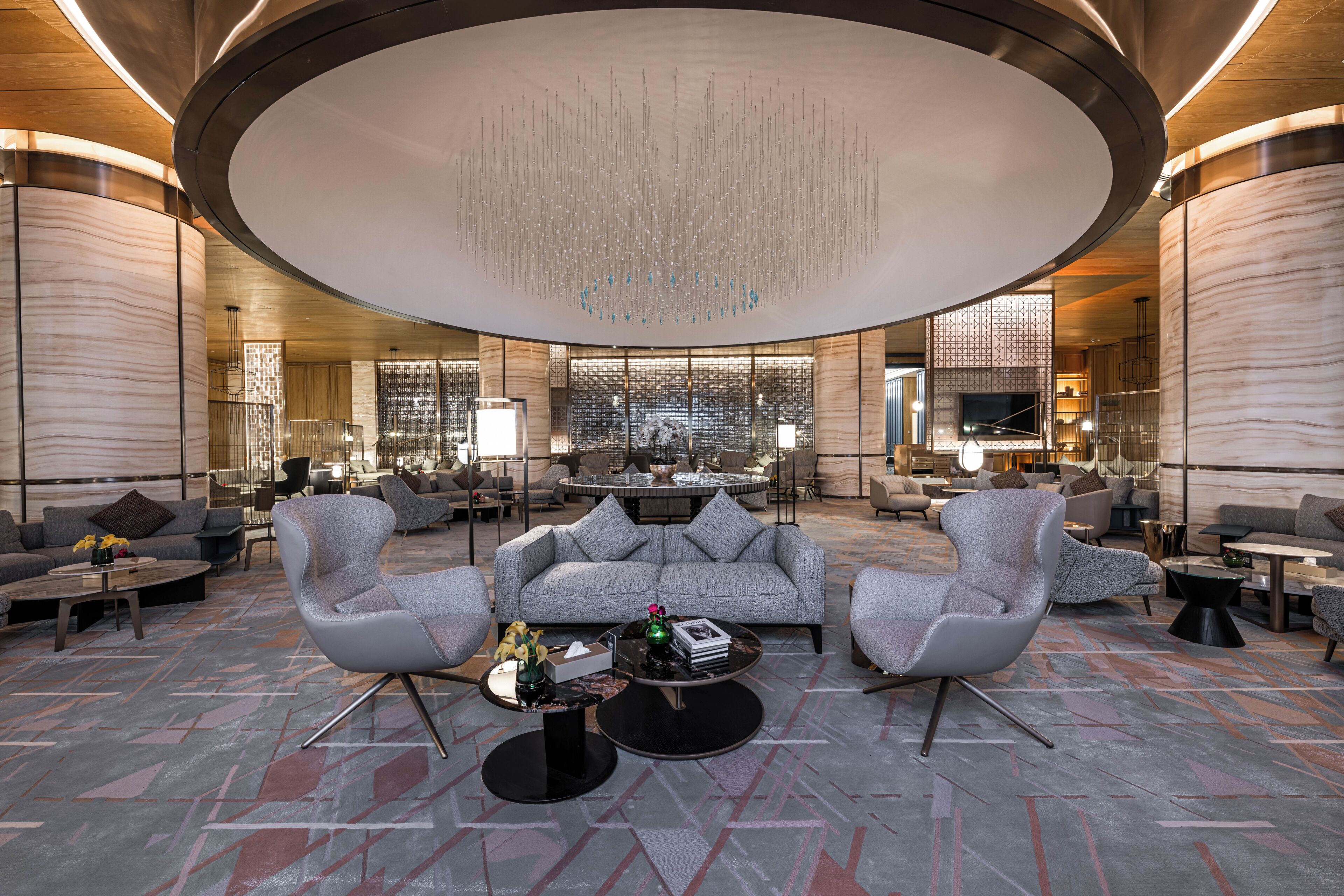 A spacious lobby with a central seating area, a high ceiling with a decorative light fixture, and a modern design.