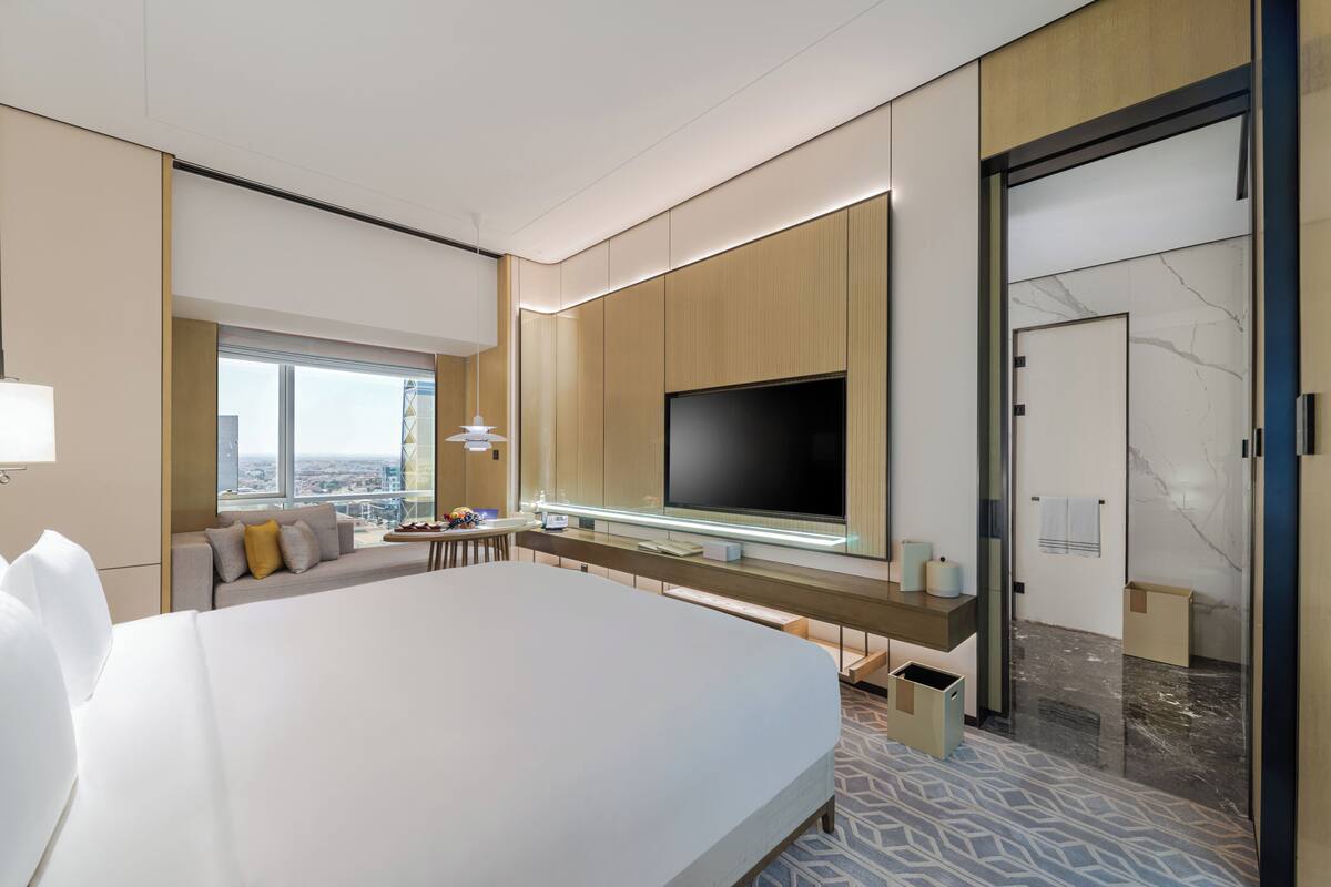 Une chambre d’hôtel moderne dotée d’un grand lit, d’un téléviseur à écran plat fixé au mur, d’un canapé et d’un bureau avec une lampe.