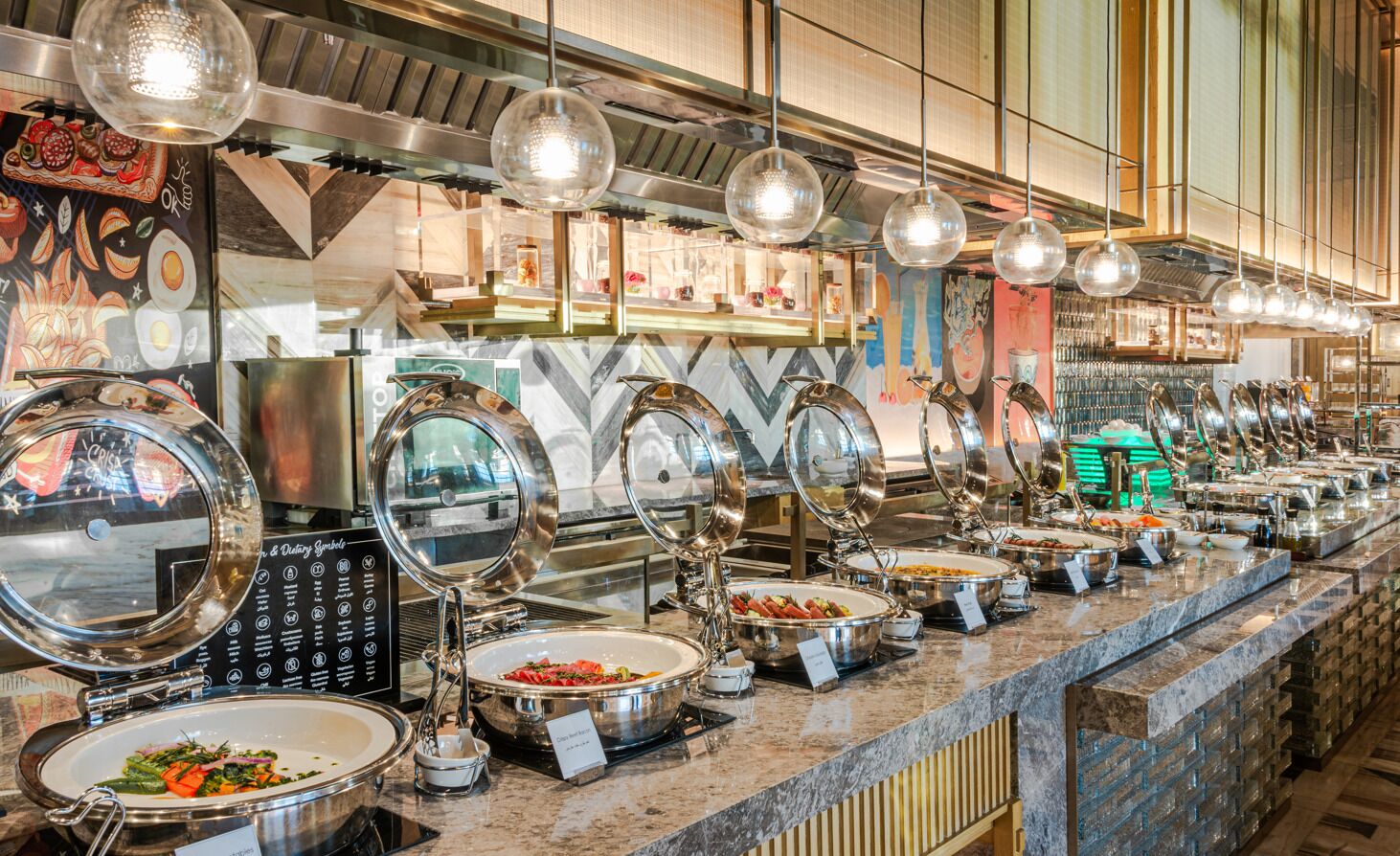 A buffet area with multiple food stations, each with a covered serving dish, and a variety of dishes displayed on the counter.