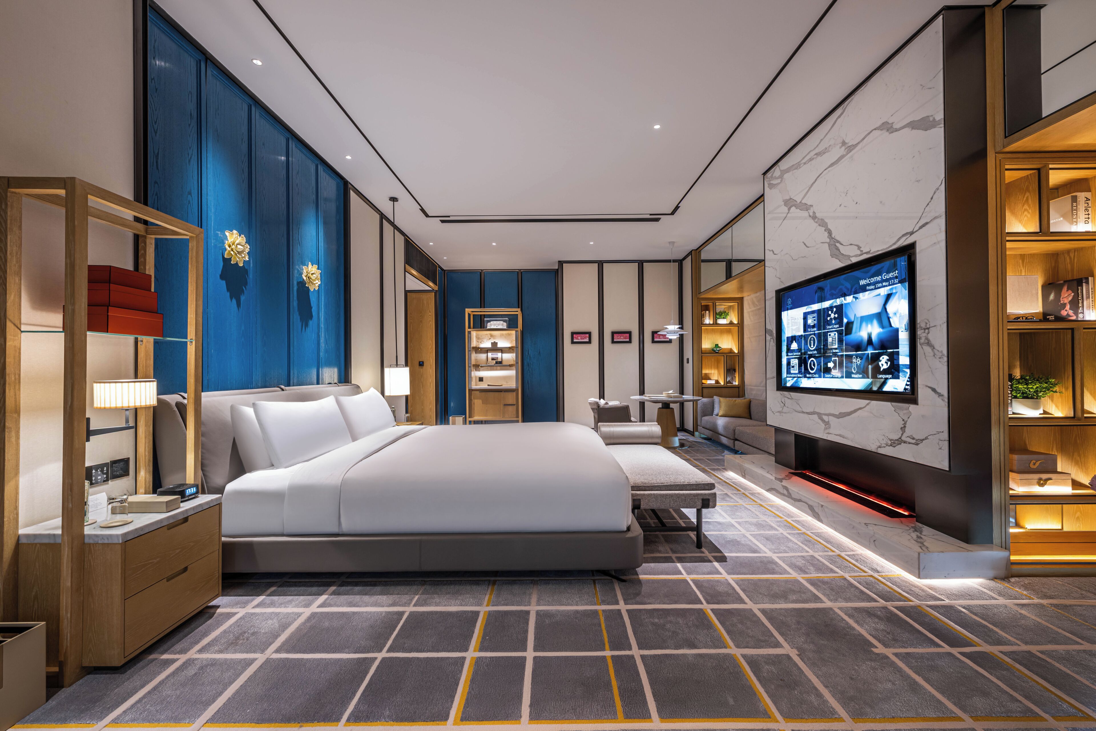 A modern hotel room with a large bed, a TV, a desk, and a seating area.
