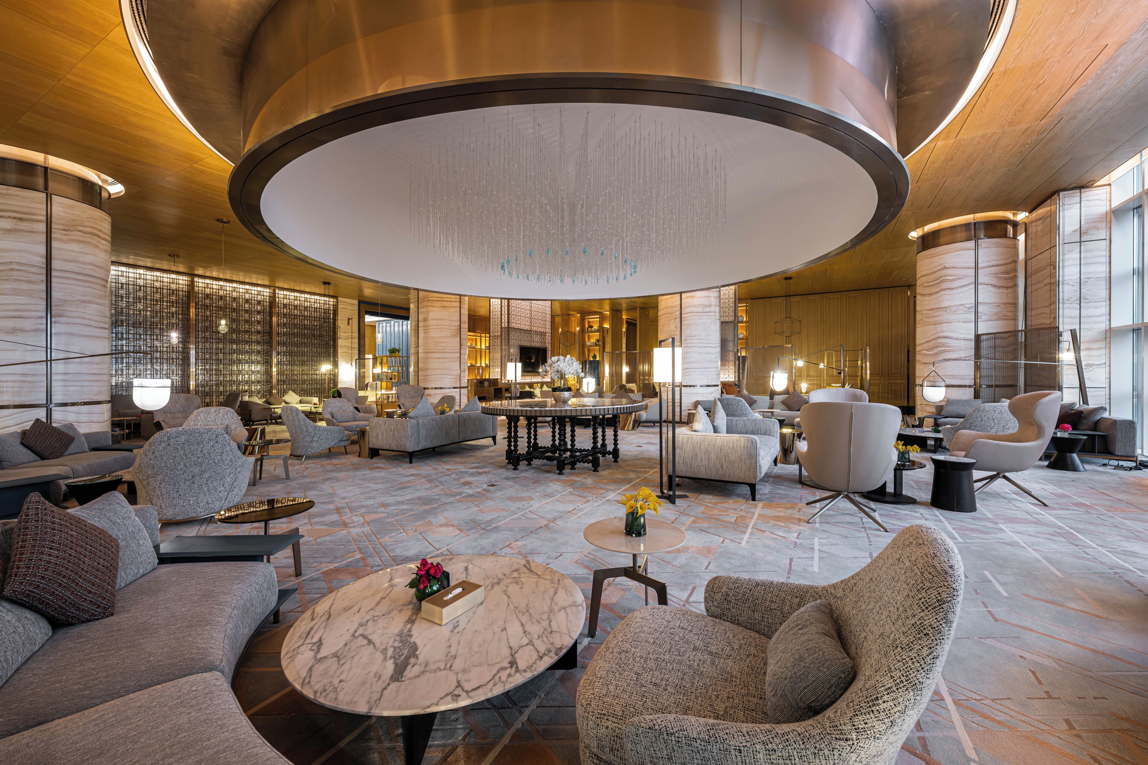 A spacious lobby with a central seating area, a fireplace, and a modern chandelier.